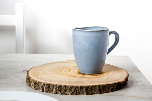 A blue ceramic cup on a wooden round cut on a beige table against a white wall. Place for text. Copy space