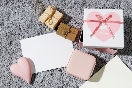 Greeting card for Valentine's Day. Envelopes, wrapped boxes, ceramic pink heart on a grey fluffy carpet background. Copy space. Place for text