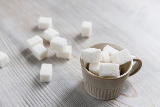 Cup with refined sugar in pieces scattered on the table