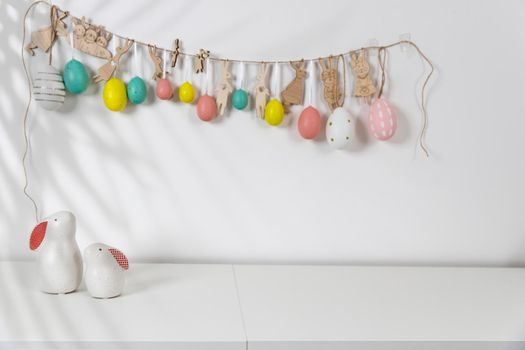 Fragment of the interior. Decorated children's room for Easter. A garland of plastic eggs on the wall. Ceramic rabbits and wooden cubes on the table. Place for your text. Easter card.