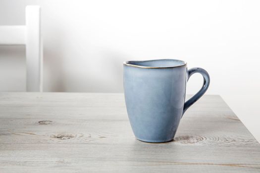 A blue ceramic cup on a beige table against a white wall. Place for text. Copy space