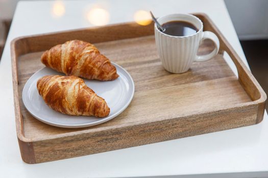 Freshly baked croissant on a gray round plate, white cup with coffee and garland on a tray on the table