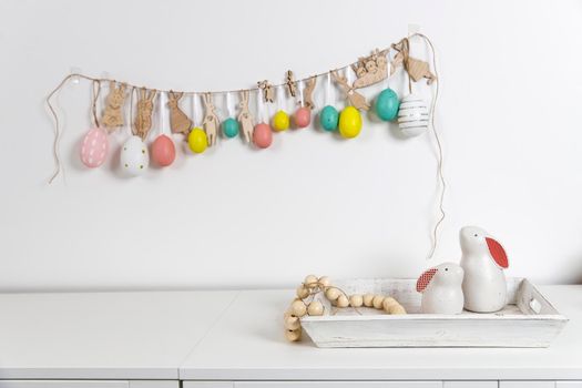Fragment of the interior. Decorated children's room for Easter. A garland of plastic eggs on the wall. Ceramic rabbits and wooden cubes on the table. Place for your text. Easter card.
