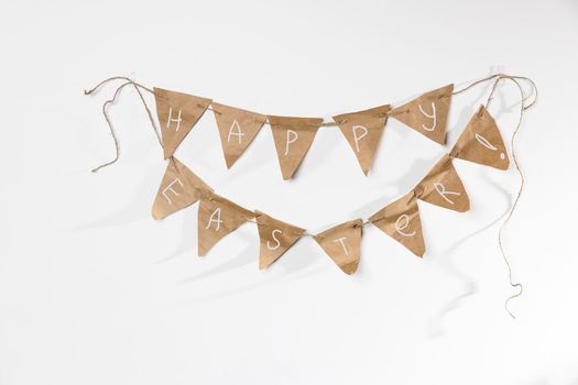 Homemade garland of craft paper flags with the inscription - Happy Easter hanging on a white wall