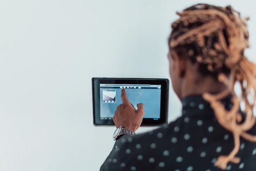 Smiling African American man using modern smart home system, controller on wall, positive young man switching temperature on thermostat or activating security alarm in apartment. High quality photo