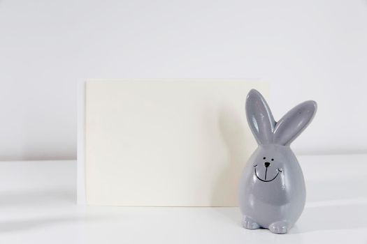 Mock up white frame with modern ceramic easter bunny decor on a shelf. White color scheme. Landscape frame orientation.