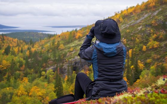 Young woman looks through binoculars and admires the mountain scenery. The traveler has his back turned to the camera. photo