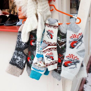 Traditional white woolen socks with knitted red bullfinches, snow maiden and deer for sale at a street market.