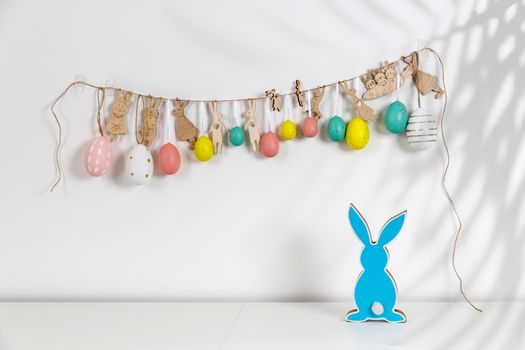 Fragment of the interior. Decorated children's room for Easter. A garland of plastic eggs and hares cut out of cardboard on the wall. Wooden blue rabbits . Place for your text. Easter card.