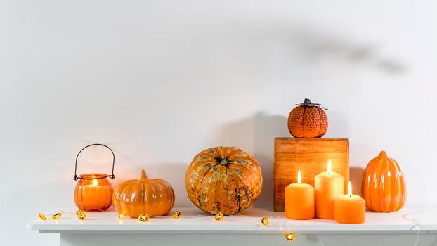 Porcelain and natural pumpkins, orange candles on a white table, Halloween decorations.