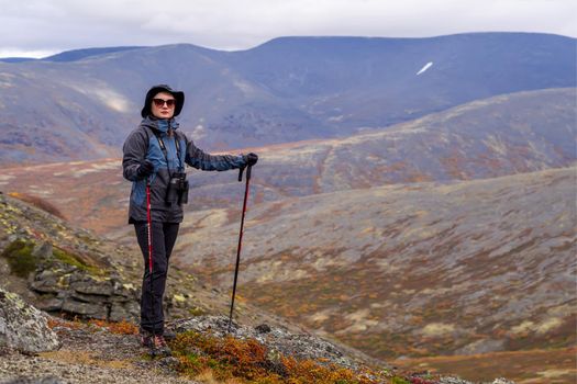 Young woman mountain tourist in glasses with trekking poles on the background of mountains.