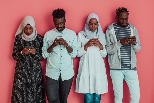 A group of African Muslim students using smartphones while standing in front of a pink background. High-quality photo