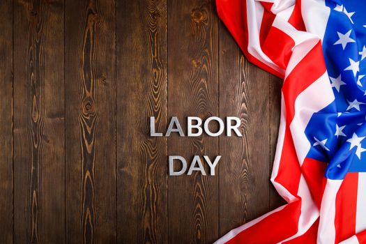 words labor day laid with silver metal letters on wooden surface with crumpled USA flag on right side in directly above high angle view