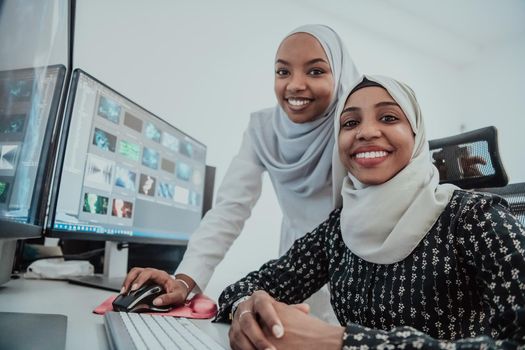 Friends at the office are two young Afro-American modern Muslim businesswomen wearing scarfs in a creative bright office workplace with a big screen. High-quality photo