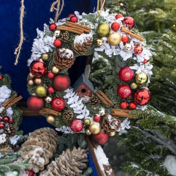 Christmas wreath of fir branches with decorations hanging on the blue wall of the house