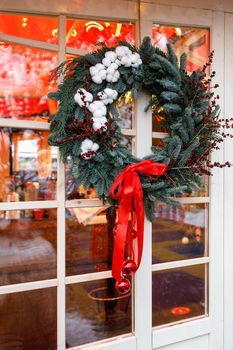 Christmas wreath of fir branches with decorations, flowers of cotton hanging on the transparent door of the house