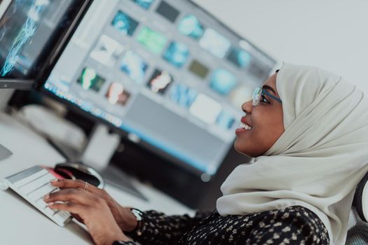 Young Afro-American modern Muslim businesswoman wearing a scarf in a creative bright office workplace with a big screen. High-quality photo