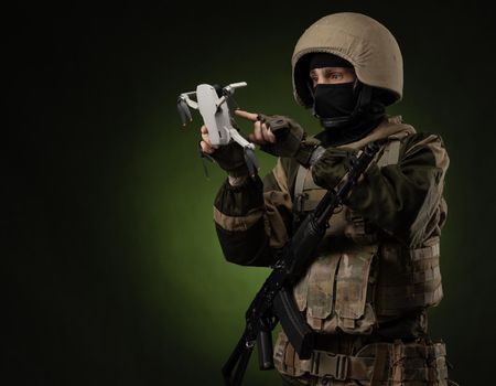 soldier in military clothes with a weapon launches a small unmanned quadcopter for reconnaissance on a dark background