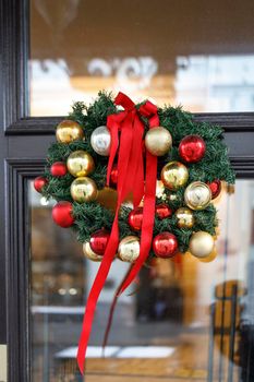 Christmas wreath of fir branches with decorations, flowers of cotton hanging on the transparent door of the house