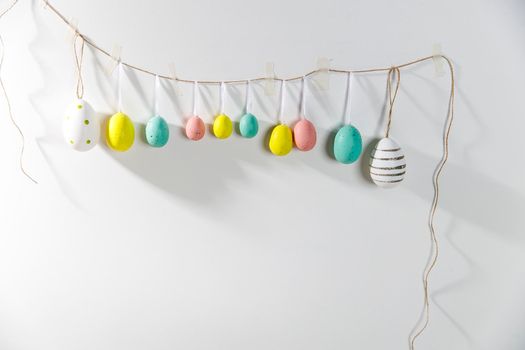 A garland of multi-colored plastic eggs hanging on a white wall. Home decoration for Easter