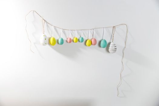 A garland of multi-colored plastic eggs hanging on a white wall. Home decoration for Easter