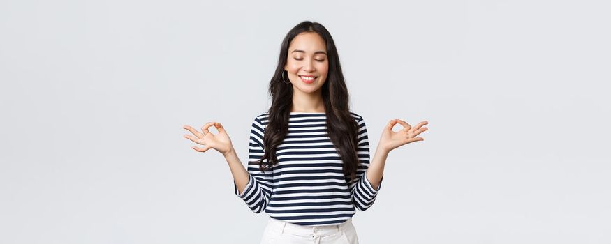 Lifestyle, people emotions and casual concept. Calm happy young woman feeling peaceful during meditation, close eyes and smiling as hold hands in zen nirvana gesture, do yoga exercise.