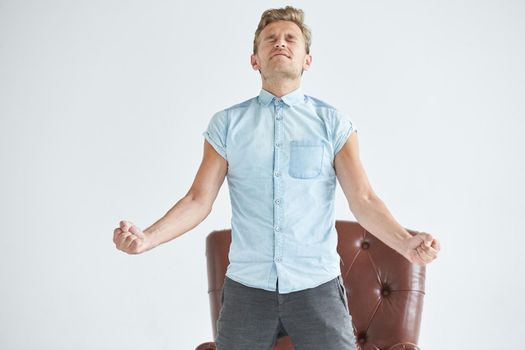 Portrait of a stylish intelligent man, small unshaven, charismatic, blue shirt, sitting on a brown leather chair, dialog, negotiation, short sleeve, brutal, hairstyle, emotions, energy, interest. High quality photo