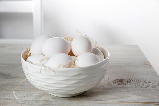 Patterned bowl with eggs on beige wooden table in white scandinavian style kitchen. Place for text. Copy space