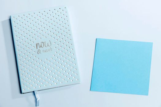 Blue notebook in a white dot with text - now or never and dark blue paper on the surface of the table. Place for your text. Concept