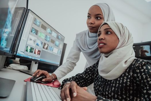 Friends at the office are two young Afro-American modern Muslim businesswomen wearing scarfs in a creative bright office workplace with a big screen. High-quality photo