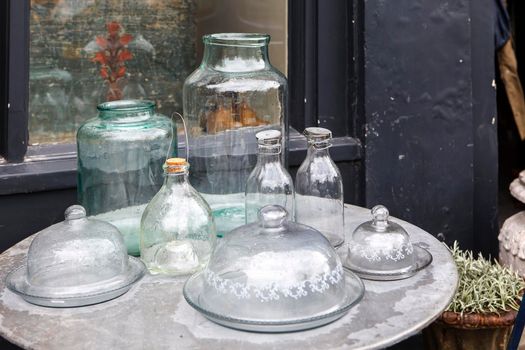 Empty milk bottles, vase, oil storage containers are on a plastic table with raindrops