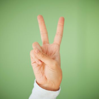 Shot of an unrecognizable woman showing the peace sign against a green background.