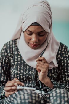 African woman using smartphone while sitting on the sofa at home wearing hijab clothes. High-quality photo