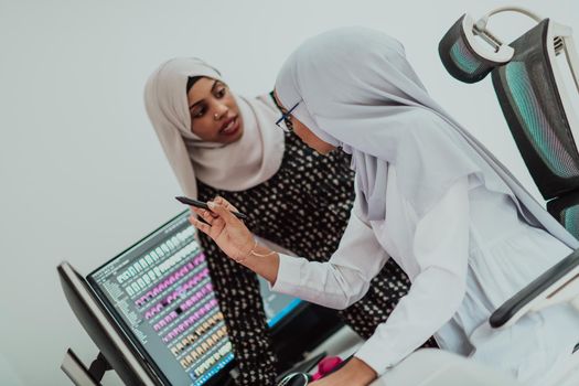 Friends at the office are two young Afro-American modern Muslim businesswomen wearing scarfs in a creative bright office workplace with a big screen. High-quality photo