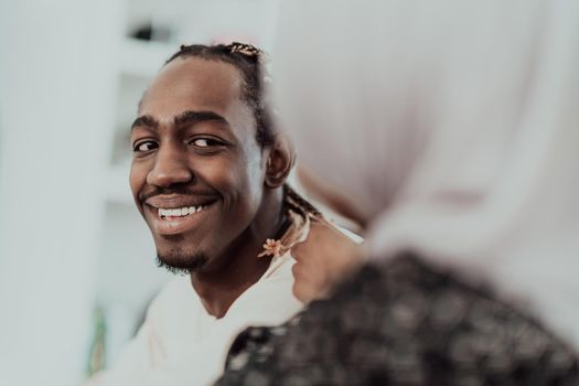 A young Muslim couple has a romantic time at home while the woman makes the hairstyle for her husband female wearing traditional Sudan Islamic hijab clothes. High-quality photo