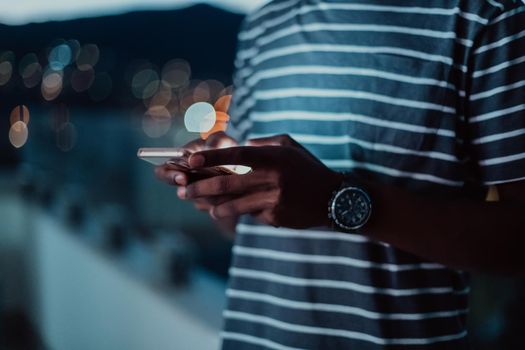 The young man on an urban city street at night texting on a smartphone with bokeh and neon city lights in the background. High-quality photo. High-quality photo