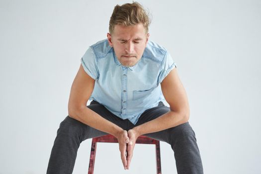 Brutal man in a shirt with short sleeves sitting on a red chair , his fists clenched , slightly bent , under the gaze of the forehead, leaned on knees, pensive, listening attentively, closed eyes. High quality photo