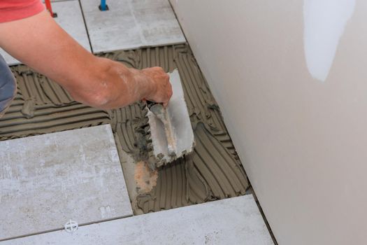Construction workers laying tile over concrete floor using tile levelers, notched trowels tile mortar