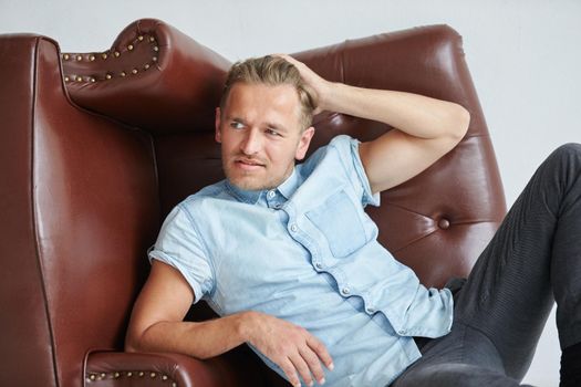 Brutal man in a shirt with short sleeves sitting in the chair, his fists clenched, slightly bent, under the gaze of the forehead. High quality photo