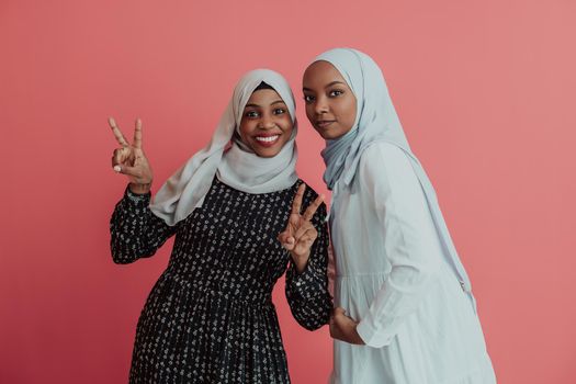 Portrait of two young modern muslim afro beauty wearing traditional islamic clothes on pink background. High quality photo
