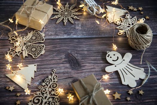 Glowing garland star, two gray boxes with gifts tied with twine, plywood Christmas decorations carved from wood on a wooden table surface. Copy space