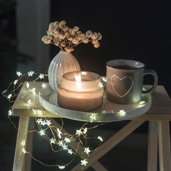A vase with white dry flowers, a gray enamel cup with a drawn heart with tea, a burning candle stand on a tray for Valentine's Day. Copy space. Place for text.