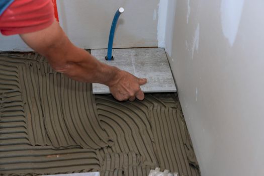 Man hands placing of worker are laying the ceramic tile on the floor