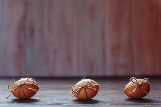 Easter beige eggs decorate with rope on brown wooden background with copyspace