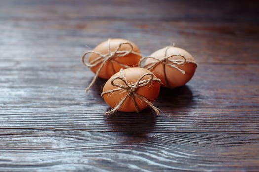 Easter beige eggs decorate with rope on brown wooden background with copyspace