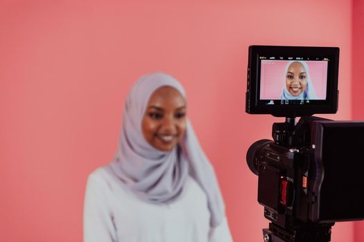 Videographer in digital studio recording video on professional camera by shooting female Muslim woman wearing hijab scarf plastic pink background. High-quality photo