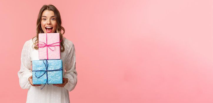 Holidays, celebration and women concept. Portrait of happy cheerful girl likes celebrating birthday and receive presents, holding two gift boxes and smiling camera, pink background.