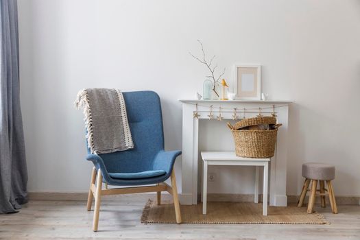 Fragment of the interior of a cozy house. A gray armchair by a white fireplace. On the fireplace is a glass bottle with a branch, figurines of birds and a photo frame. Place for text