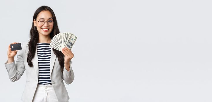 Business, finance and employment, entrepreneur and money concept. Successful asian businesswoman showing explain on courses how increase income, hold credit card and money, smiling camera.