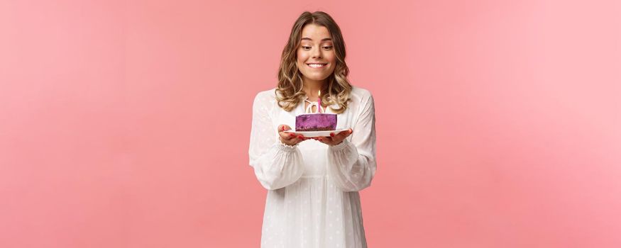 Holidays, spring and party concept. Portrait of dreamy, happy birthday girl feeling excitement and joy celebrating b-day, biting lip and smiling as making wish blowing candle on cake.